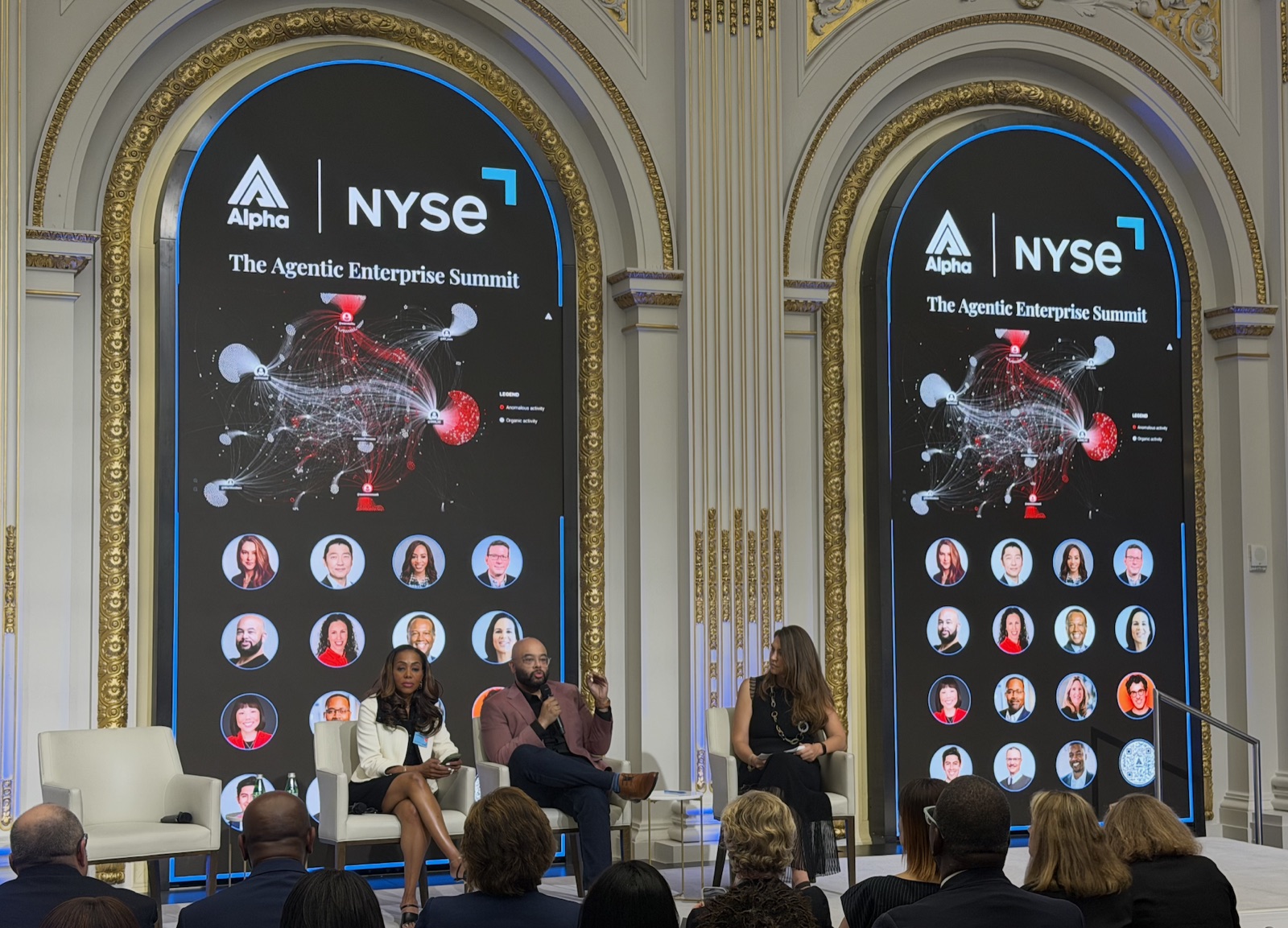 A panel seated before a large agentic network visualization at the Alpha and NYSE summit.